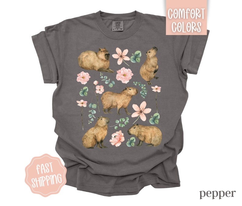 Pu&ograve; includere: Una t-shirt grigio antracite con una stampa di capibara e fiori rosa. I capibara sono marroni e hanno delle macchie bianche. I fiori sono rosa e bianchi.