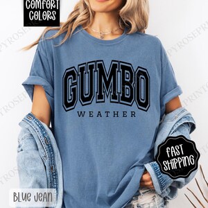 May include: A blue t-shirt with the text "GUMBO WEATHER" in black block letters.