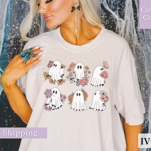 May include: A white t-shirt with a graphic of six ghosts holding flowers and butterflies. The ghosts are in a pastel color palette. The text "Comfort Colors" is in the upper right corner of the image. The text "IVORY" is in the lower right corner of the image.