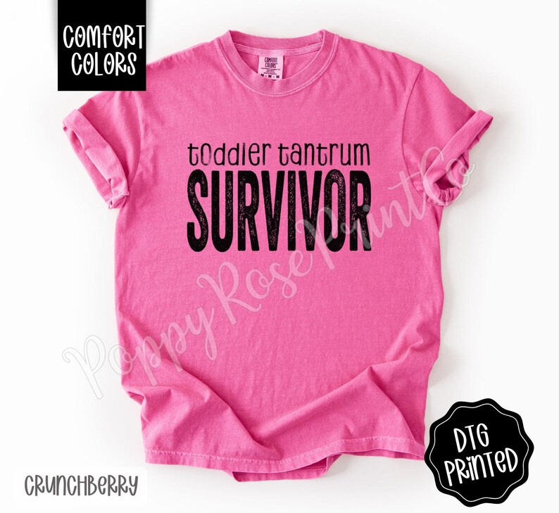 May include: A bright pink t-shirt with the words "toddler tantrum SURVIVOR" in black block letters. The shirt has short sleeves and a crew neck. The words "Comfort Colors" are in a black box in the upper left corner.