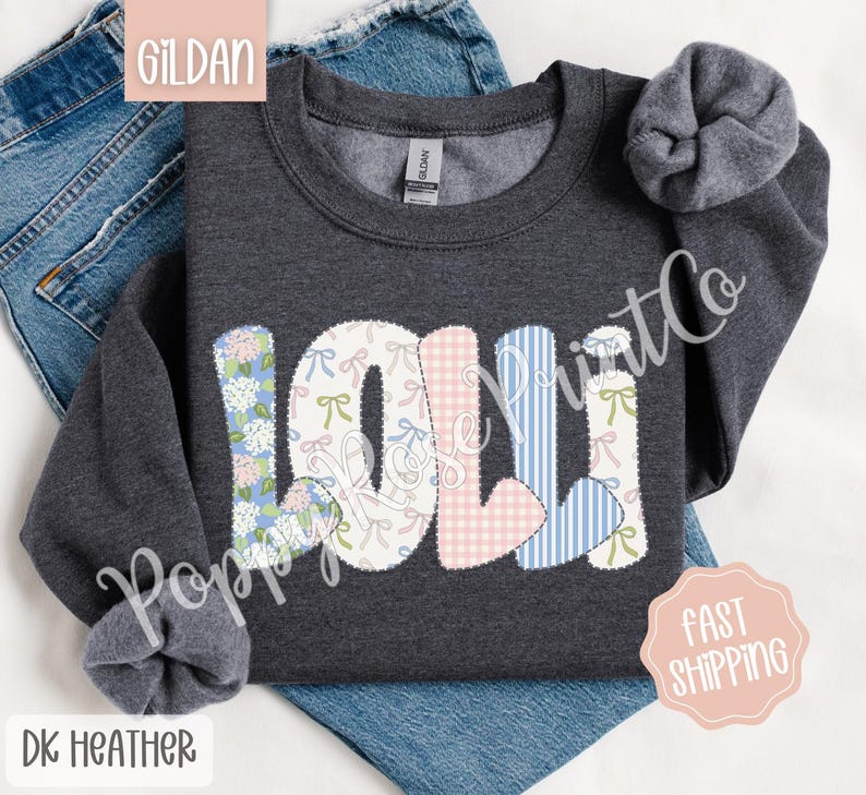 May include: Dark heather grey sweatshirt with the name "Lolli" spelled out in colorful patchwork letters. Each letter is decorated with a different floral pattern, including pink gingham, blue stripes, and white with pink bows.