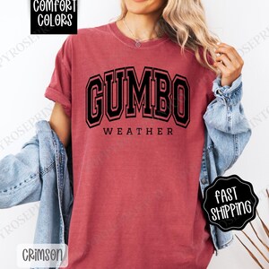 May include: A red t-shirt with the text "GUMBO WEATHER" in black block letters. The shirt is made of a soft, comfortable material.