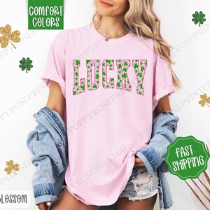 May include: Pink t-shirt with the word "LUCKY" in green and pink letters. The letters are filled with a pattern of green shamrocks.