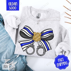May include: A gray sweatshirt with a blue and black ribbon bow with a gold police badge that says "Back the Blue" hanging from the center.  The bow is tied with handcuffs.