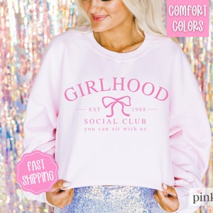 May include: Pink cropped sweatshirt with the text "GIRLHOOD EST 1988 SOCIAL CLUB you can sit with us" and a pink bow.