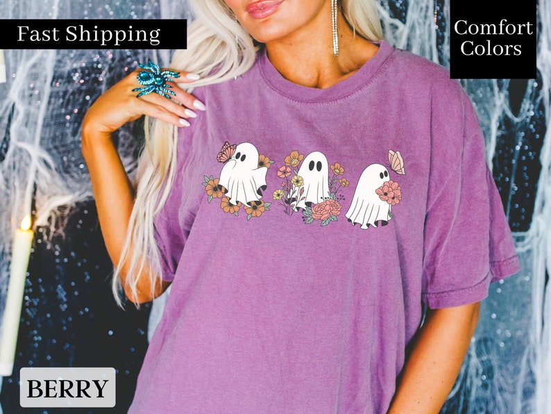 Peut inclure: Un t-shirt violet avec un motif de trois fant&ocirc;mes tenant des fleurs. Les fant&ocirc;mes sont blancs et les fleurs sont roses, orange et jaunes. Le texte "Fast Shipping" est dans le coin sup&eacute;rieur gauche de l'image et le texte "Comfort Colors" est dans le coin sup&eacute;rieur droit de l'image.
