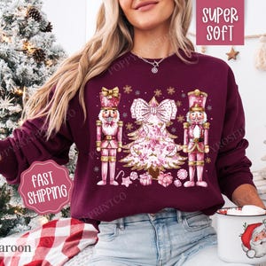 May include: Burgundy sweatshirt with a pink Christmas tree and two nutcracker figures. The text "Super Soft" is on a white tag and the text "Fast Shipping" is on a white tag.