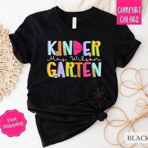 May include: Black t-shirt with the text "Kinder Mrs. Wilson Garten" in colorful letters. The letters are decorated with school supplies and other designs.