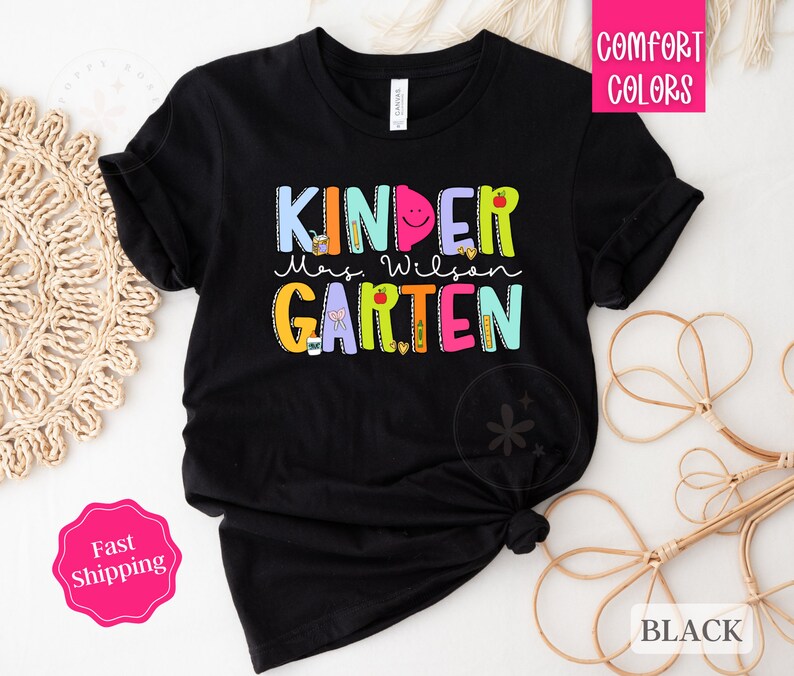 May include: Black t-shirt with the text "Kinder Mrs. Wilson Garten" in colorful letters. The letters are decorated with school supplies and other designs.