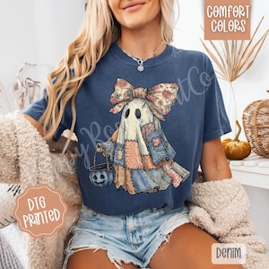 May include: Navy blue t-shirt featuring a patchwork ghost with a floral bow, holding a pumpkin bucket. The design includes various fabric patterns and colors. The shirt has the words "Comfort Colors" and "Denim" printed on it.