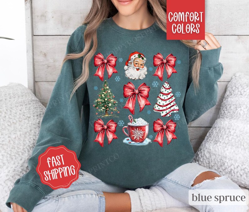 May include: A teal blue sweatshirt with a Christmas theme featuring Santa Claus, a Christmas tree, red bows, and a cup of hot chocolate. The text "Comfort Colors" and "Fast Shipping" are also visible on the sweatshirt.
