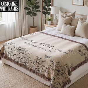 May include: Beige woven throw blanket with a floral design and the names "Henry & Olivia" and the date "SEPTEMBER 4 2025" in black script. The blanket has a fringed edge and is draped over a bed.