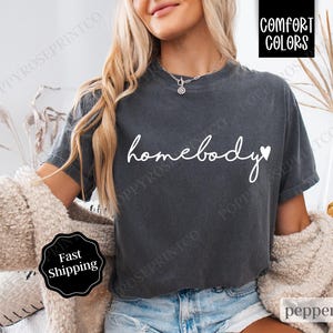 May include: A dark gray t-shirt with the text "homebody" in white with a small white heart after the word "body".