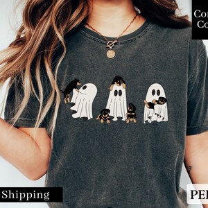 May include: A dark gray t-shirt with a graphic of four Rottweiler puppies dressed as ghosts. The text "Comfort Colors" is in the upper right corner of the image. The text "PEPPER" is in the lower right corner of the image.