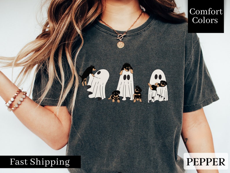 May include: A dark gray t-shirt with a graphic of four Rottweiler puppies dressed as ghosts. The text "Comfort Colors" is in the upper right corner of the image. The text "PEPPER" is in the lower right corner of the image.