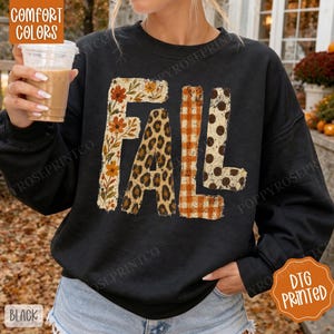 Peut inclure: Un sweat-shirt noir à manches longues avec le mot FALL imprimé en grandes lettres. Chaque lettre présente un motif distinct : le F a un imprimé floral, le A un imprimé léopard, et les L présentent des carreaux orange et blanc et des pois.