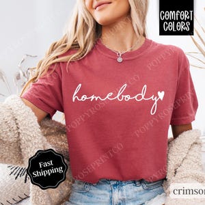 May include: A red t-shirt with the text "homebody" in white with a small heart next to it.
