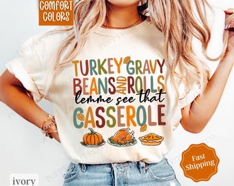 Könnte beinhalten: Ein weißes T-Shirt mit dem Text "TURKEY GRAVY BEANS AND ROLLS lemme see that CASSEROLE" in bunten Buchstaben. Das Shirt zeigt ein Thanksgiving-Design mit Illustrationen von einem Truthahn, einem Kürbis und einer Auflaufform.