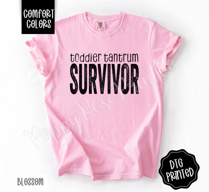 May include: A light pink t-shirt with the words "toddler tantrum SURVIVOR" printed in black. The shirt has rolled-up sleeves and the words "COMFORT COLORS" and "BLOSSOM" are printed on the shirt.