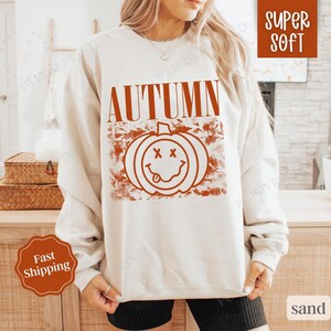 May include: A white sweatshirt with the text "AUTUMN" in orange letters and a smiling pumpkin graphic with a red outline. The sweatshirt is super soft and comfortable.