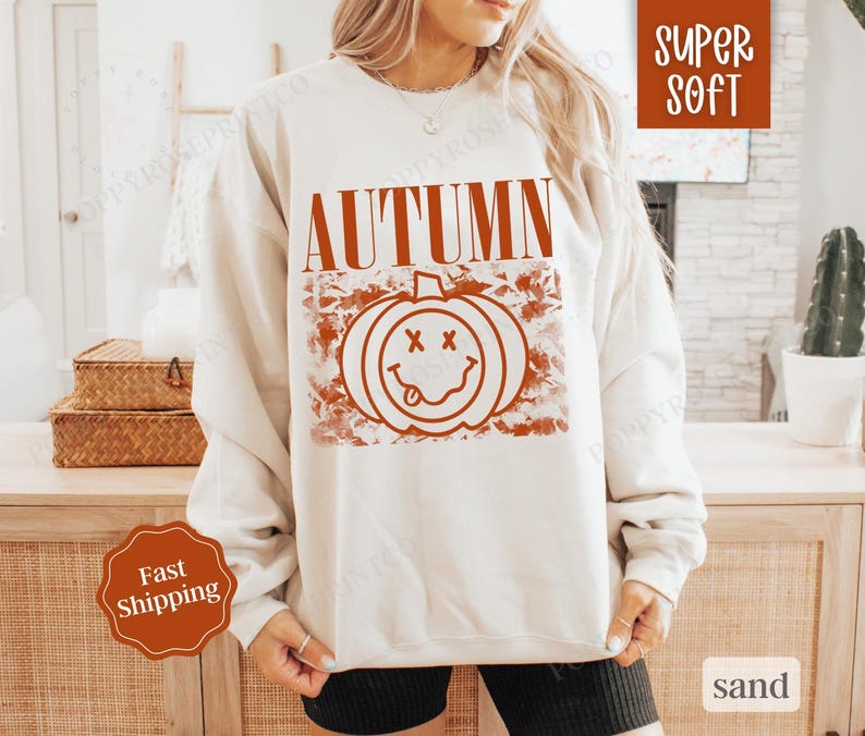 May include: A white sweatshirt with the text "AUTUMN" in orange letters and a smiling pumpkin graphic with a red outline. The sweatshirt is super soft and comfortable.