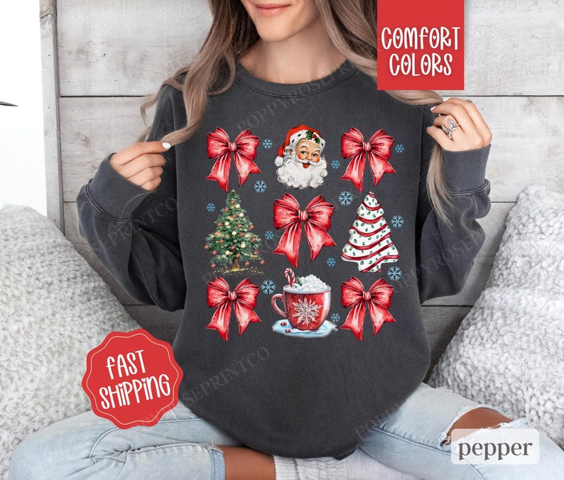 May include: A dark gray sweatshirt with a Christmas theme featuring Santa Claus, Christmas trees, bows, and a cup of hot chocolate. The text "Comfort Colors" is visible in the upper right corner of the image.