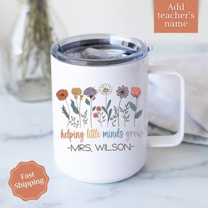 Może przedstawiać: Biały kubek podr&oacute;żny z uchwytem i kwiatowym wzorem. Kubek zawiera napis "helping little minds grow" i "-MRS. WILSON-". Projekt zawiera kolorowe kwiaty w kolorze pomarańczowym, ż&oacute;łtym, fioletowym i r&oacute;żowym.
