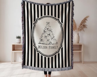 May include: Black and white striped throw blanket with a decorative Christmas tree design. The tree is adorned with bows and the text "WILSON FAMILY" is below the tree. The blanket has a fringed edge.