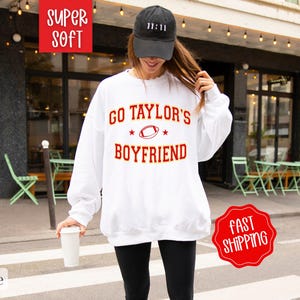 May include: White sweatshirt with the text "Go Taylor's Boyfriend" in red and a football graphic. The sweatshirt is super soft and has a relaxed fit.