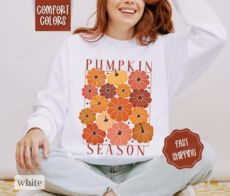 May include: White sweatshirt with the text "Pumpkin Season" in a retro font. The text is surrounded by a graphic of orange, red, and brown pumpkins.