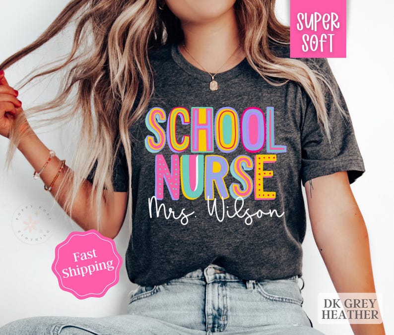 Puede incluir: Una camiseta de color gris jaspeado oscuro con el texto "SCHOOL NURSE Mrs. Wilson" en letras de colores y contorneadas. La camiseta es s&uacute;per suave y tiene un corte holgado.