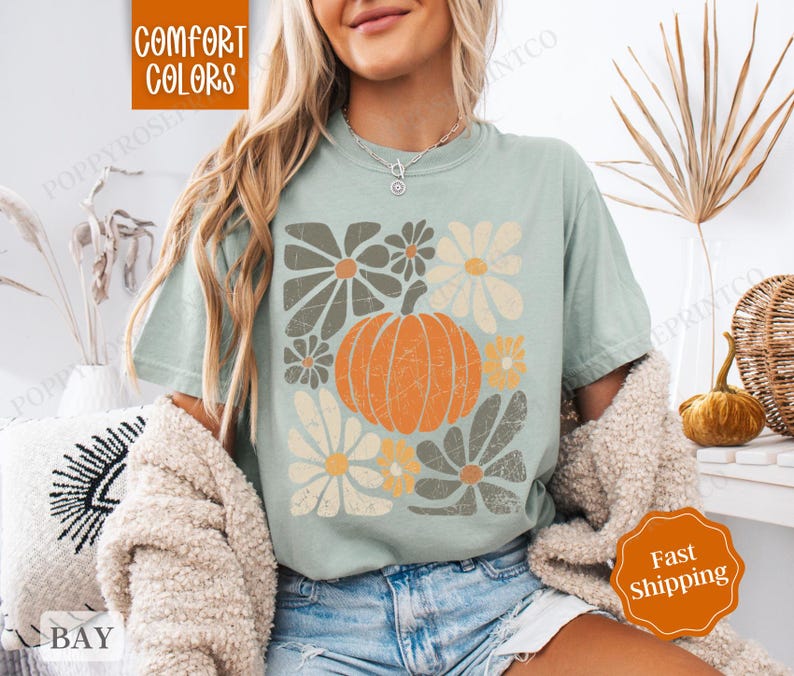 Puede incluir: Una camiseta azul claro con un dise&ntilde;o floral y una calabaza. El texto "Comfort Colors" est&aacute; impreso en la camiseta.