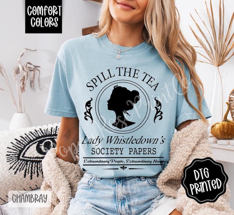 Pu&ograve; includere: T-shirt azzurra con la scritta "SPILL THE TEA" e "Lady Whistledown's SOCIETY PAPERS". La maglietta presenta una silhouette nera del profilo di una donna all'interno di un disegno circolare. La maglietta &egrave; in tessuto chambray.