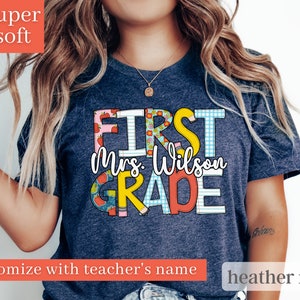 May include: A heather navy blue t-shirt with the text "First Grade" in colourful, patterned letters. The text "Mrs. Wilson" is included in the design.
