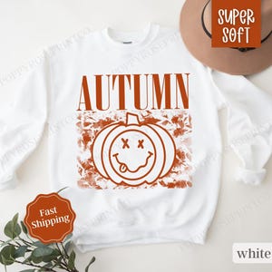 May include: White sweatshirt with a brown graphic of a smiling pumpkin with the word "AUTUMN" above it.