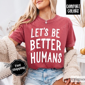 May include: A crimson red t-shirt with the text "Let's Be Better Humans" printed in white.
