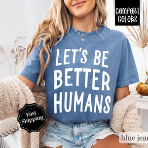 May include: A blue jean t-shirt with the text "Let's Be Better Humans" in white lettering.