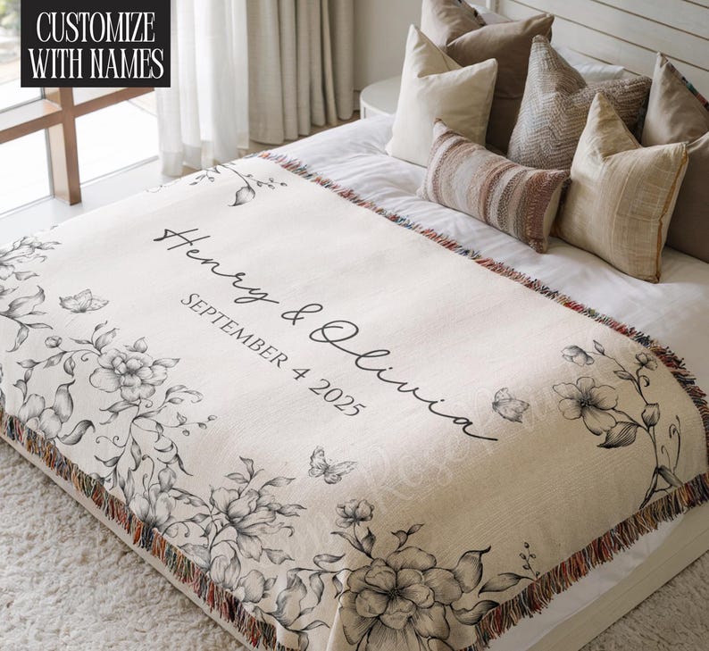 May include: Cream-colored throw blanket with floral and butterfly illustrations. The blanket features the names "Henry & Olivia" and the date "SEPTEMBER 4 2025" in black script. The text "CUSTOMIZE WITH NAMES" is in the upper left corner.