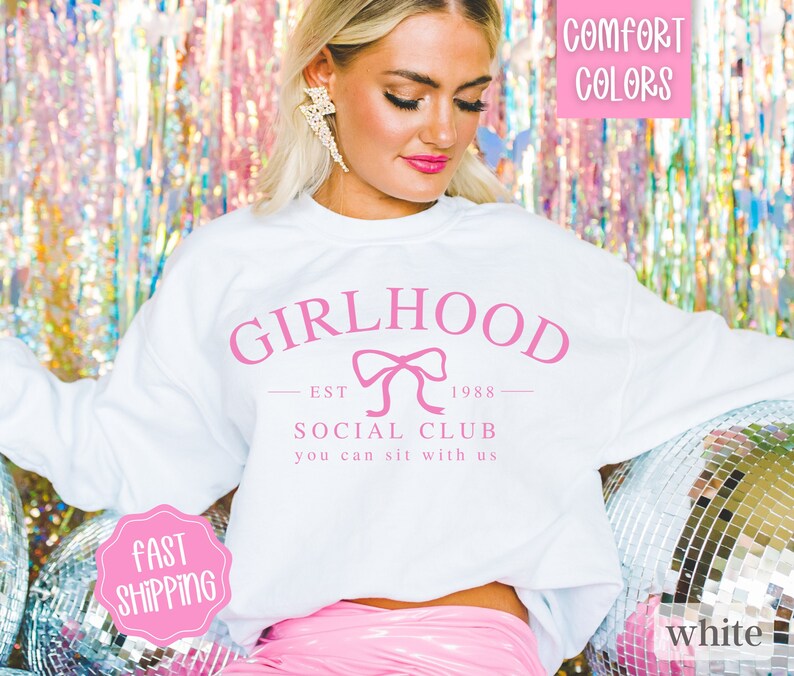 May include: White sweatshirt with pink text that reads "GIRLHOOD EST 1988 SOCIAL CLUB you can sit with us" and a pink bow graphic.