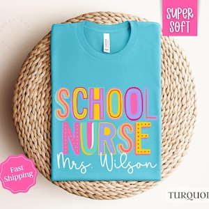 Puede incluir: Camiseta azul turquesa con el texto "School Nurse Mrs. Wilson" en letras de colores. La camiseta est&aacute; hecha de tela s&uacute;per suave.