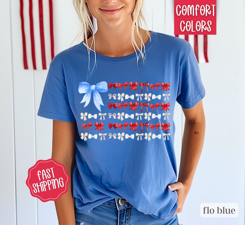 May include: Flo blue t-shirt with a bow and ribbon design in red, white, and blue. The shirt has the words "Comfort Colors" and "flo blue" printed on it. The shirt also has a "Fast Shipping" sticker.