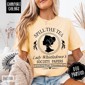 Pu&ograve; includere: T-shirt color burro con la scritta "Spill the Tea" e la silhouette nera del profilo di una donna in un cerchio. La maglietta presenta anche il testo "Lady Whistledown's Society Papers" e "Extraordinary People, Extraordinary News."