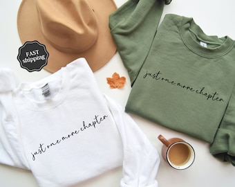 May include: Two long-sleeved sweatshirts with the text "just one more chapter" in black script. One sweatshirt is white and the other is green.