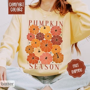 May include: A yellow sweatshirt with the text "Pumpkin Season" and a graphic of stylized pumpkins in shades of orange, red, and brown.