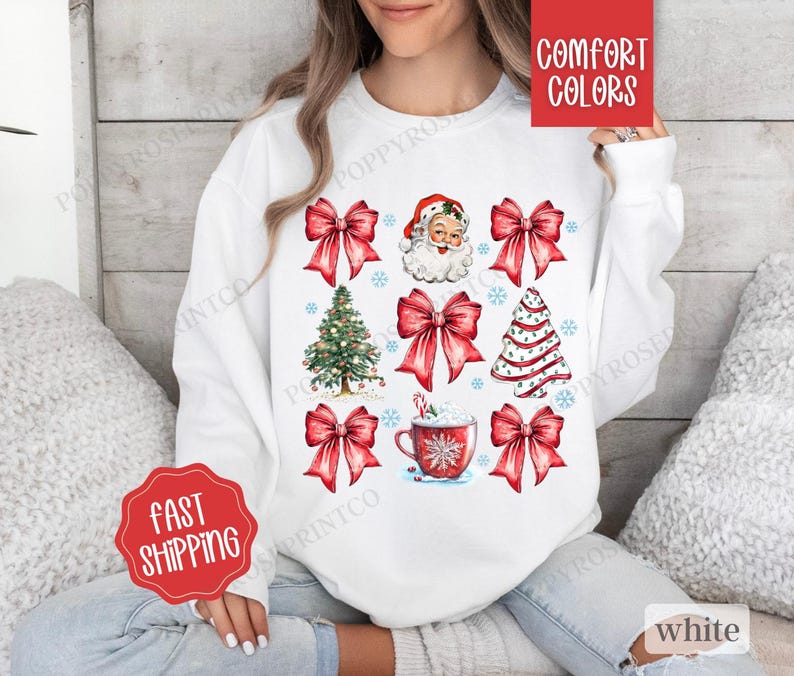 May include: White sweatshirt with a Christmas theme featuring red bows, a Santa Claus face, a Christmas tree, and a cup of hot chocolate. The text "Comfort Colors" is on a red tag attached to the sweatshirt.