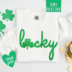 May include: White sweatshirt with a green glitter "lucky" design. The design includes a shamrock.