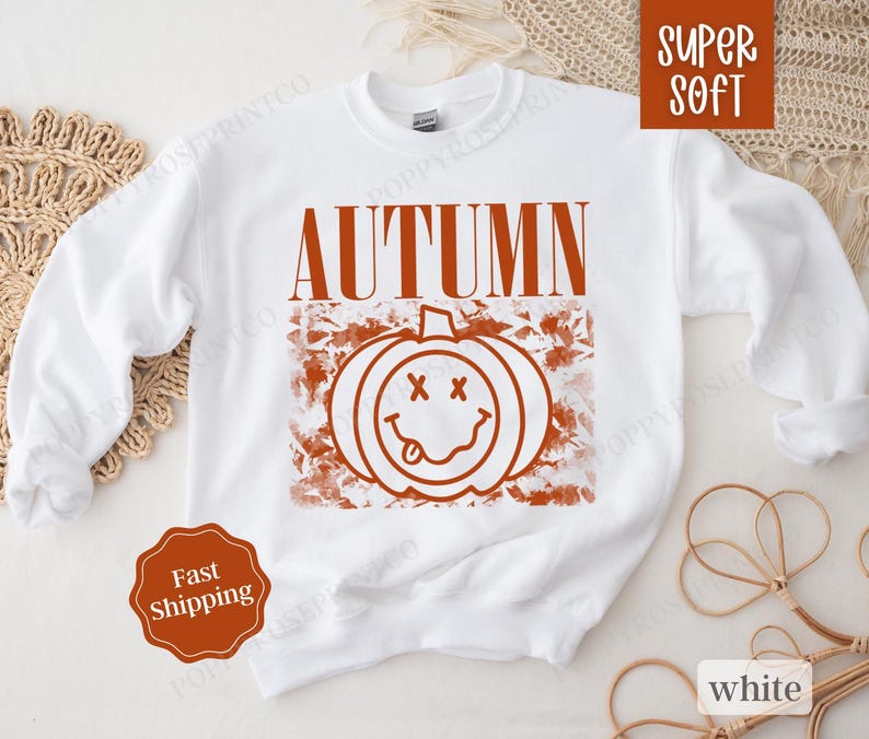 May include: White sweatshirt with the text "AUTUMN" in orange and a graphic of a smiling pumpkin with a tongue sticking out.