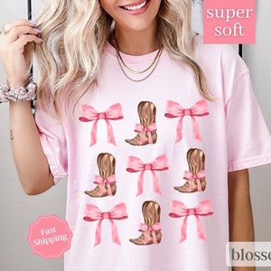 May include: Pink t-shirt with a graphic of brown cowboy boots and pink bows. The text "super soft" and "blossom" are on the shirt.