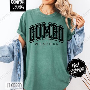 May include: A green t-shirt with the text "GUMBO WEATHER" in black block letters. The shirt is made of a soft, comfortable material.
