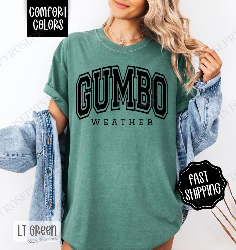 May include: A green t-shirt with the text "GUMBO WEATHER" in black block letters. The shirt is made of a soft, comfortable material.